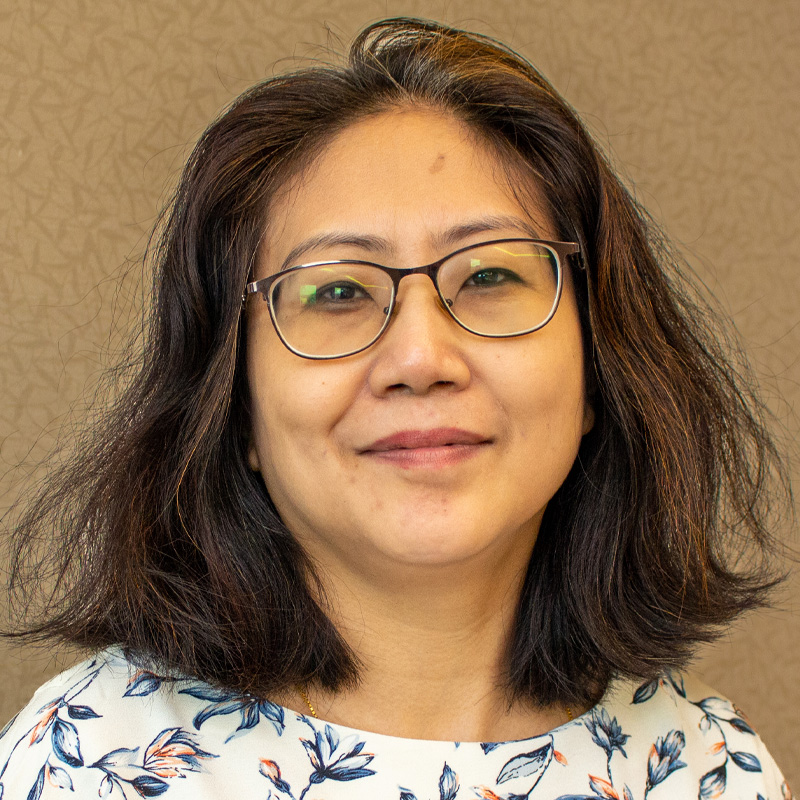 asian woman with glasses and dark brown hair, wearing a boat neck patterned top. She's looking straight at the camera.