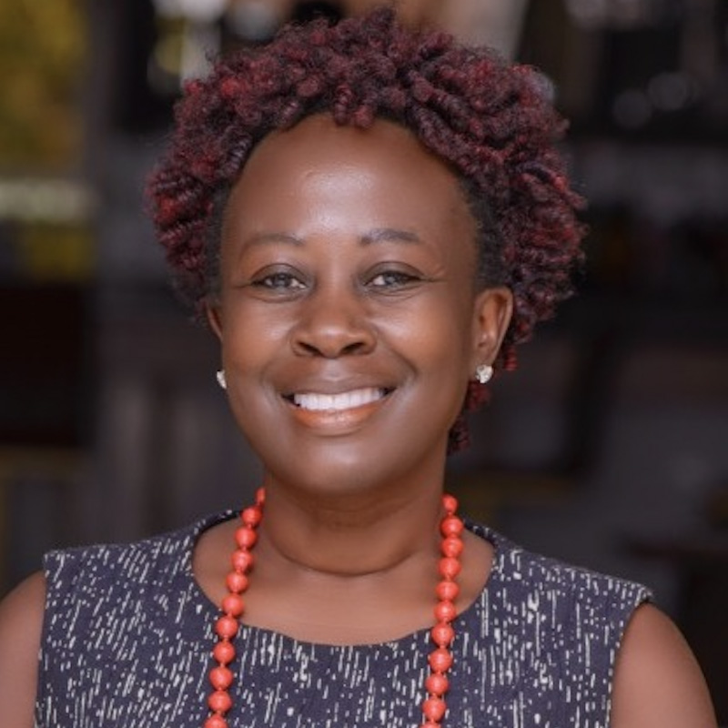 Black woman with reddish/brown curly hair, sleeveless black and white top, orange beads, and she's smiling at the camera